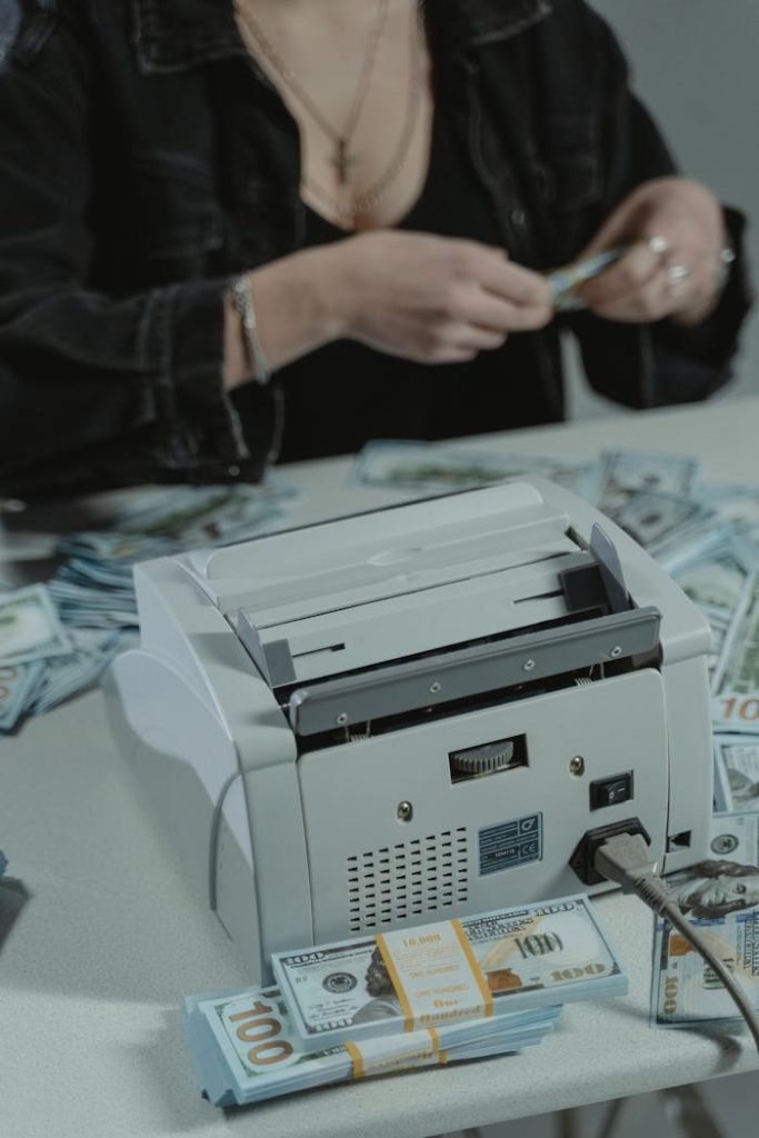 Woman Sitting at Table with Banknotes and Money Counter